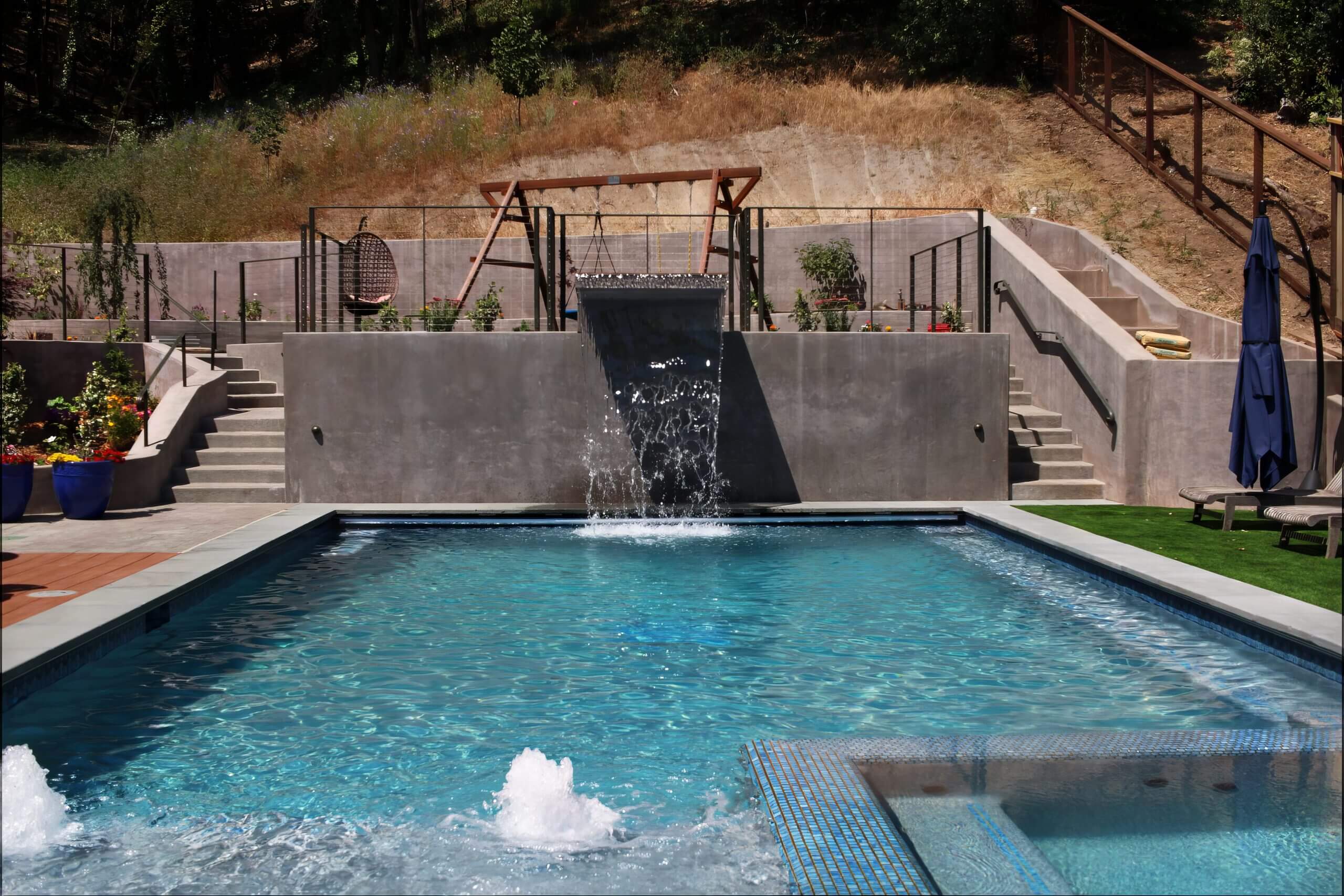 Modern outdoor pool with waterfall feature and spa area.